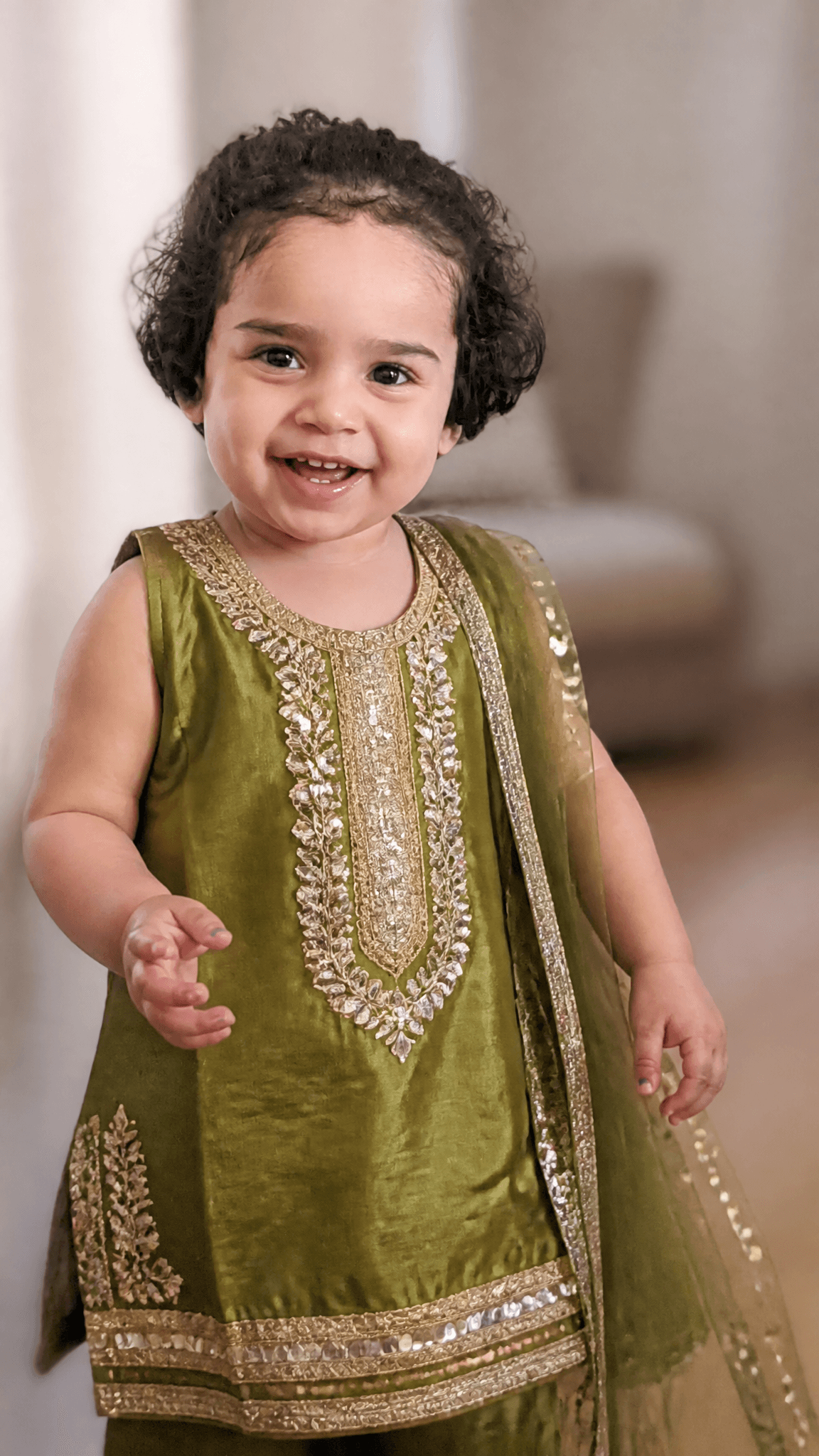 A joyful toddler stands in a brightly lit indoor space, wear