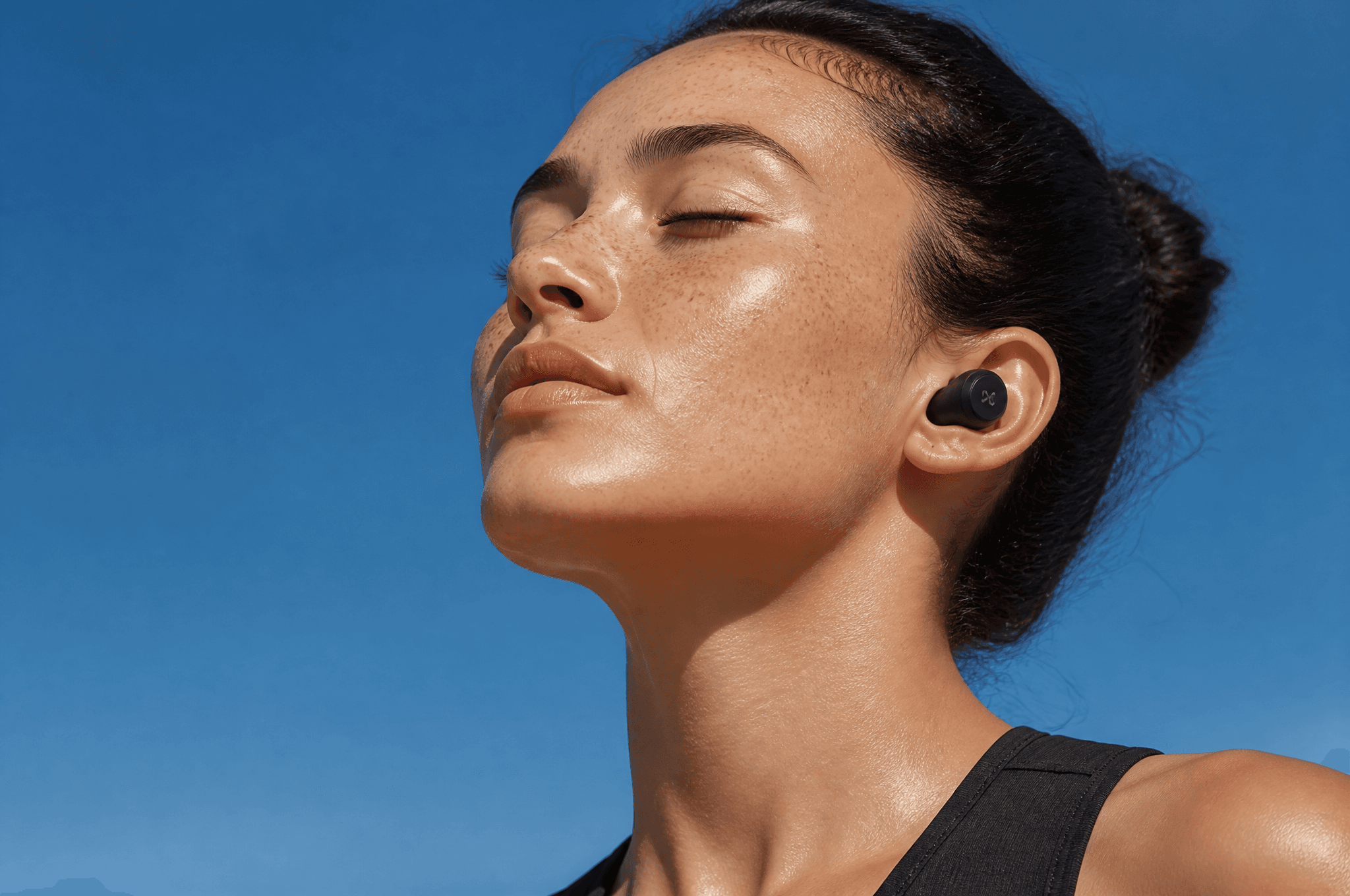 A serene close-up of a freckled woman with wireless earbuds,