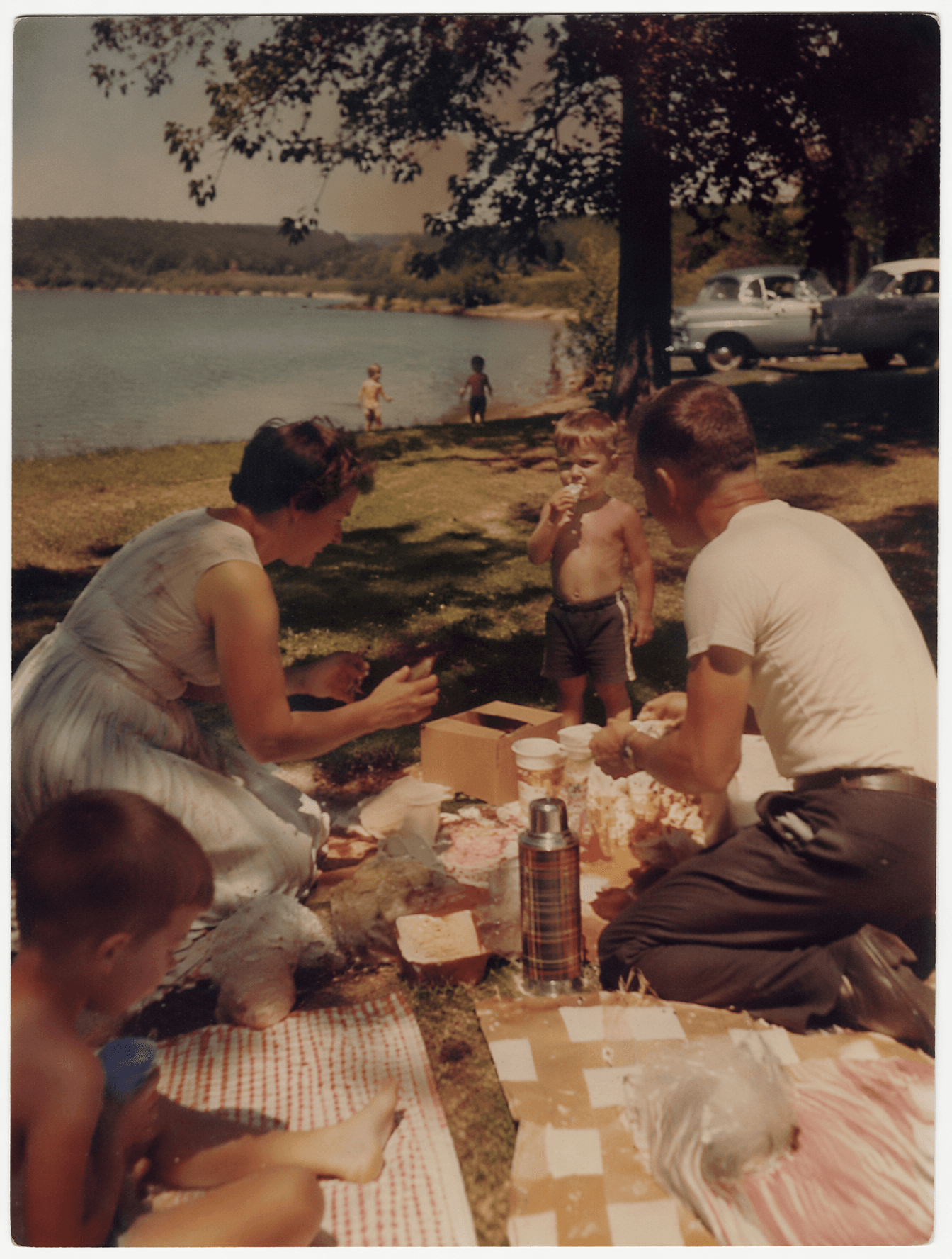 1950s family picnic beside a peaceful lake, adults preparing