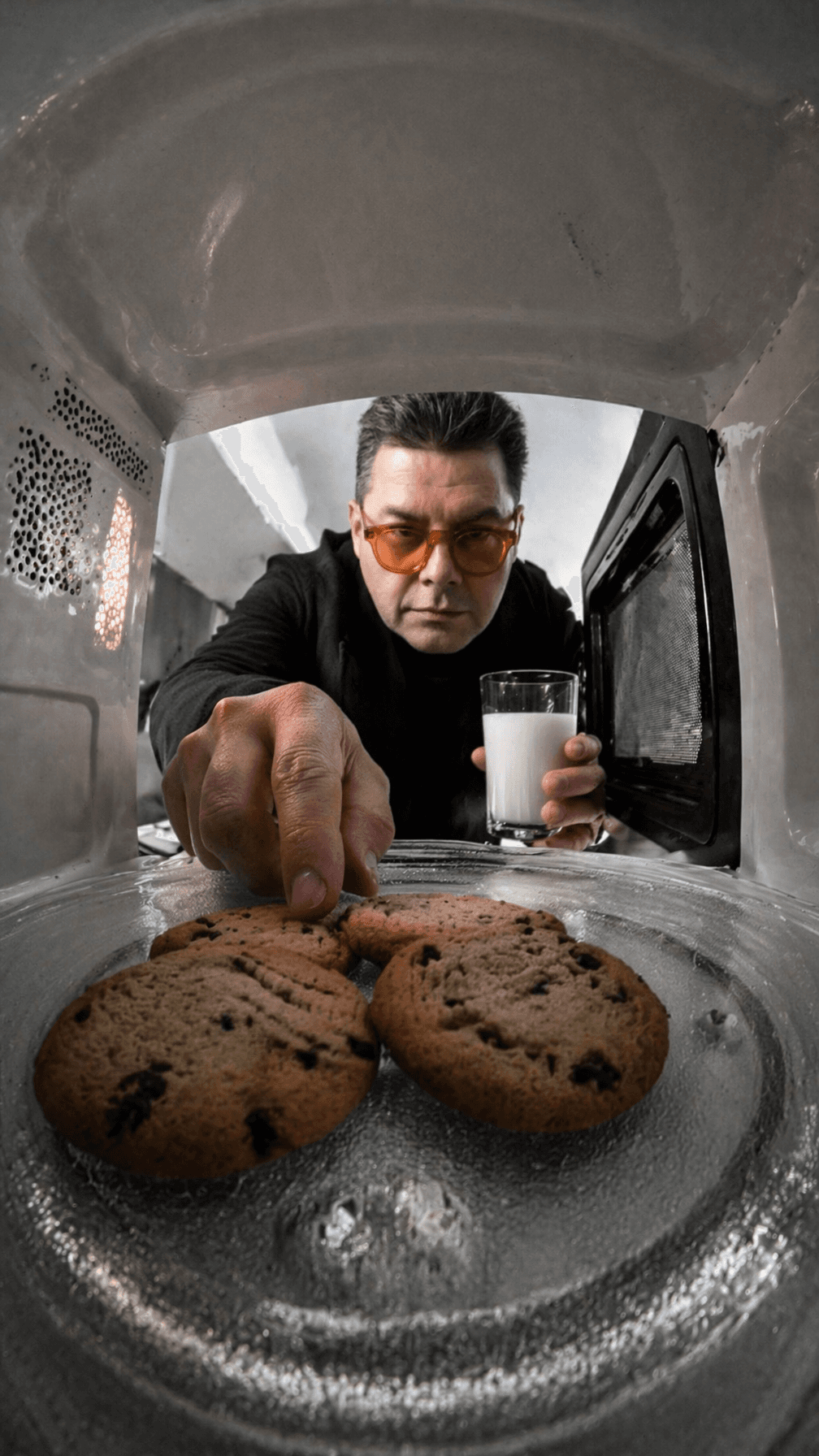A person reaching into a microwave for cookies while holding