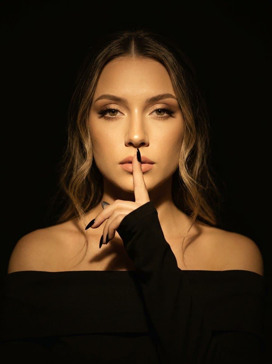 A woman stands in a dark room, her body facing the camera, h