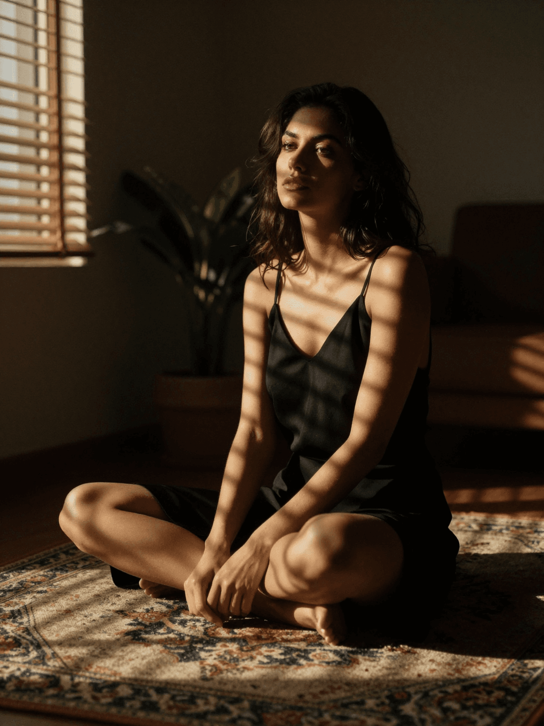 A woman sits cross-legged on a patterned rug within a dimly 