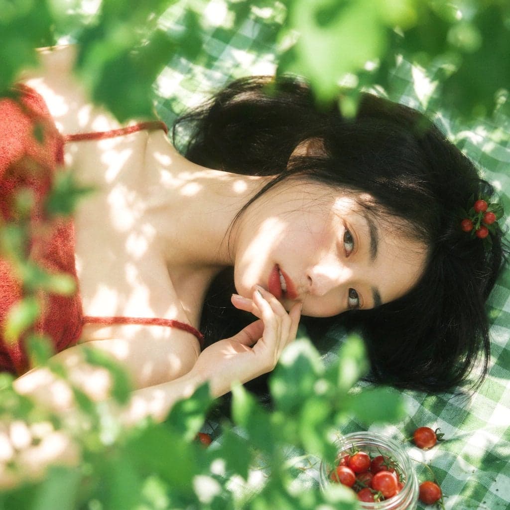 真人摄影，夏日植物系生活方式写真，清透日系胶片感，竖幅 2:3，俯拍近景到面部特写，年轻女性横向躺在绿白格纹野餐布上，脸