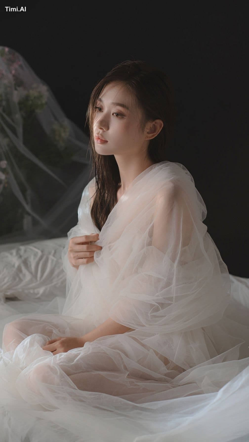 一位20多岁的年轻成年东亚女性侧身坐在铺有白色床单的床上，画面从头顶拍至膝部附近。人物位于中央略偏右，身体以三分之二侧面